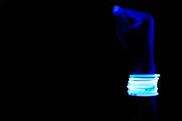 Fist with glow bracelets under ultraviolet light.