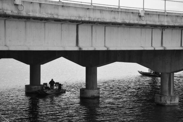 Florence, AL, 2020: Distant shot of single fisherman in boat under new Shoal Creek Bridge