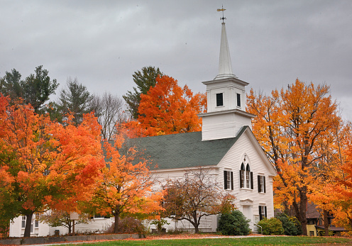 Autumn in scenic New England. Colorful orange and red maple trees framing First Unitarion Congregational Church in rural Wilton Center, New Hampshire.