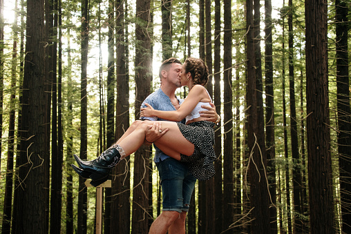 A young couple in a forest. The man picks up the woman as they kiss