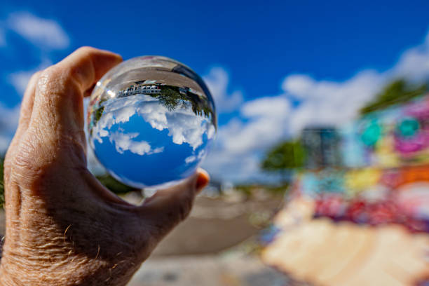 istock Lens ball held by male hand reflecting a blue sky with white clouds, green trees with a wall with an explosion of colors 1269363893