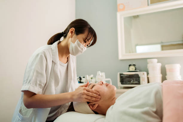 Asian chinese female beautician doing face treatment for her customer at facial beauty salon stock photo