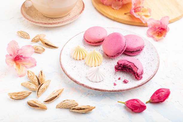 istock Purple macarons or macaroons cakes with cup of coffee on a white concrete background decorated with flowers. Side view, close up. 1269372859