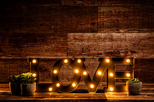 This is a front view photograph of a Love sign lit up with tiny edison light bulbs on a antique retr wood table background