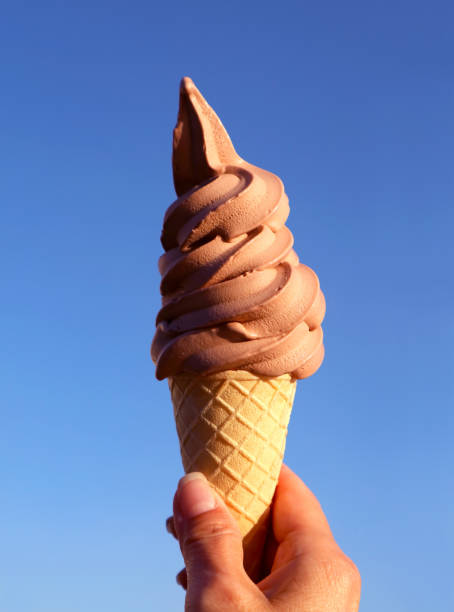 istock Hand Holding a Chocolate Soft Serve Ice Cream Cone Against Sunny Blue Sky 1269375711