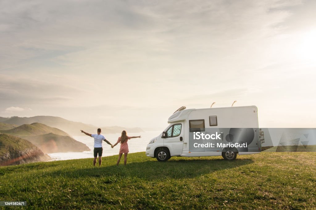 Young couple traveling with their motor home standing by the sea with arms raised Motor Home Stock Photo