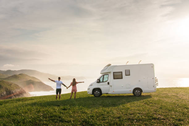 Young couple traveling with their motor home standing by the sea with arms raised Young couple traveling with their motor home standing by the sea with arms raised cantabria stock pictures, royalty-free photos & images