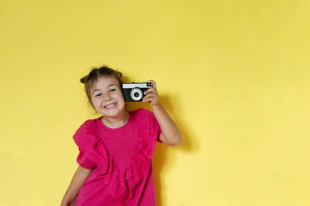 Small girl taking picture with retro camera isolated on yellow background