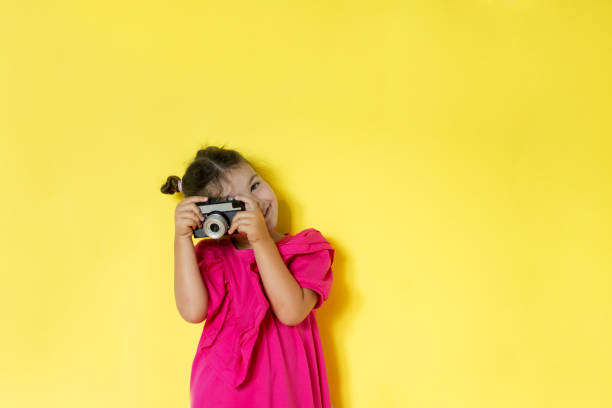 Small girl taking picture with retro camera isolated on yellow background
