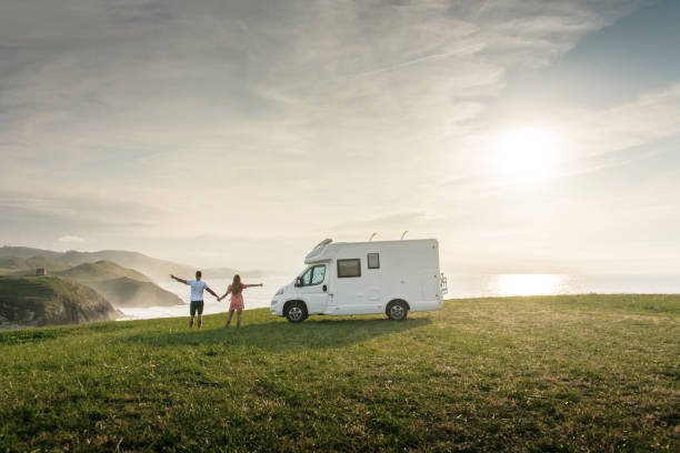 young couple traveling with their motor home standing by the sea with arms raised - rv imagens e fotografias de stock