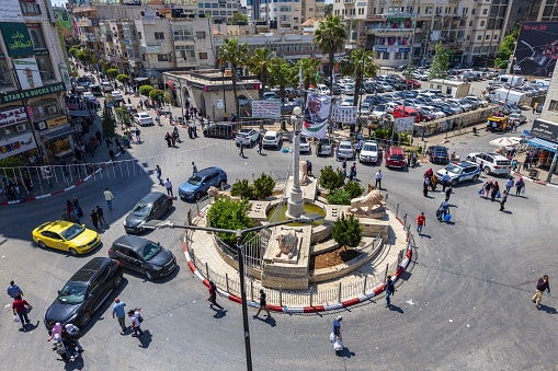 Ramallah, Palestine, May 4, 2019: The people walk through Al-Manara Square in the center of Ramallah. This circular square is dominated by a monument with a stone pillar surrounded by five stone lions who are described as a traditional symbol symbols of bravery, power and pride.