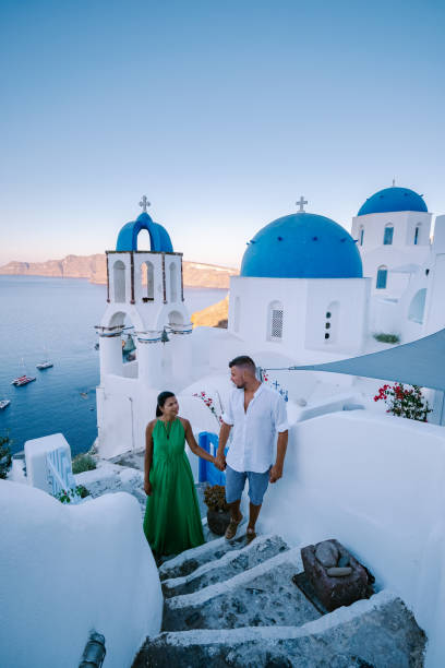 Santorini Greece, young couple on luxury vacation at the Island of Santorini watching sunrise by the blue dome church and whitewashed village of Oia Santorini Greece during sunrise, men and woman on holiday in Greece Santorini Greece, young couple on luxury vacation at the Island of Santorini watching sunrise by the blue dome church and whitewashed village of Oia Santorini Greece during sunrise during summer vacation, men and woman on holiday in Greece greece travel stock pictures, royalty-free photos & images