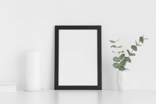 istock Black frame mockup with workspace accessories and eucalyptus in a vase on a white table. Portrait orientation. 1269393955