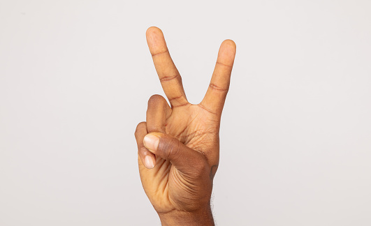 Black male hand making peace sign front of white background.
