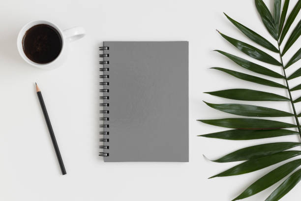 istock Top view of a grey notebook mockup with  workspace accessories and a palm leaf on a white table. 1269394831