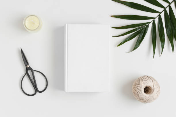 istock Top view of a white book mockup with  workspace accessories and a palm leaf on a white table. 1269394849