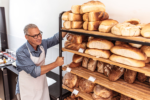 Photo of mature Handsome worker in uniform carrying shelves with bread at the bakery manufacturing.