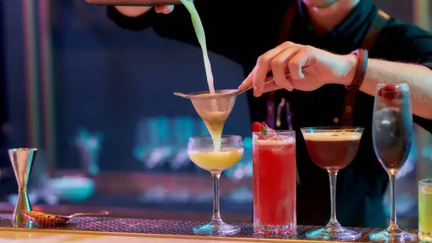 Photo of Fresh up your night. Close up of hands of male bartender pouring, mixing ingredients while making cocktails, alcoholic drinks at the bar counter in the night club