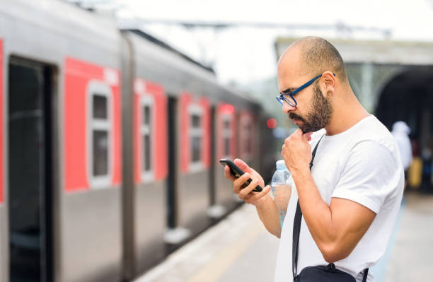 Checking for the next train online Shot of a young man standing on railway station with a mobile phone commuter train photos stock pictures, royalty-free photos & images