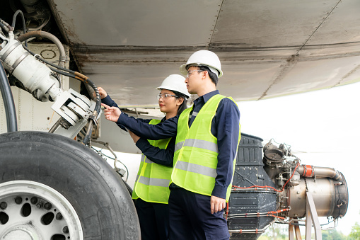 Asian man and woman engineer maintenance airplane team repairs, fixes, modernization and renovation in front airplane from  in airport.