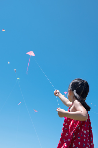 Little girl flying a kite high up in blue sky view from behind