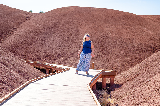 Fashionable blonde woman hikes and walks through the Painted Cove red rock area boardwalks in John Day Fossil Beds National Monuent - Painted Hills Unit