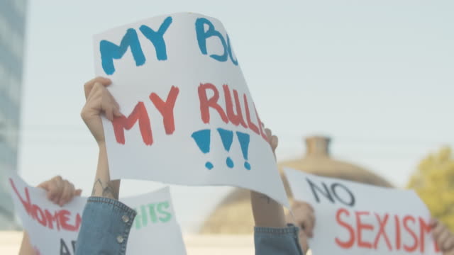 Close-up of My body my rules poster in female Caucasian hands. Unrecognizable young feminist holding banner with anti-sexism slogan on demonstration against gender discrimination. Cinema 4k ProRes HQ.