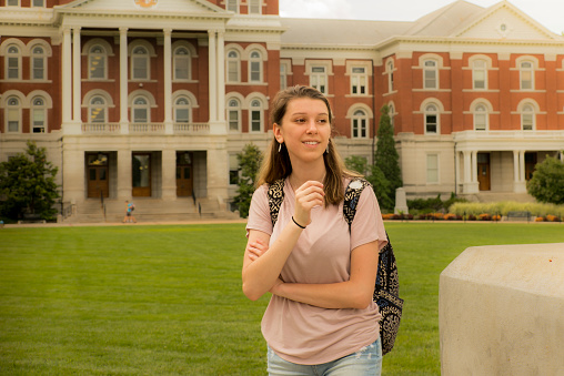 Environmental portrait of smiling female student with backpack in late afternoon; Midwestern university building in the background