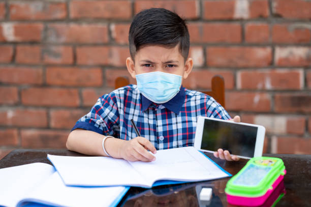 Little kid attending class of school wearing face mask and uniform. Education and schooling in corona virus pandemic. Little kid attending class of school wearing face mask and uniform. Education and schooling in corona virus pandemic. Covid 19 or Coronavirus and Air pollution pm2.5 concept - telephone voip dust internet stock pictures, royalty-free photos & images