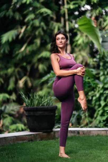 Woman practicing yoga performing yoga-asanas outdoors. Young attractive slim fitness girl in bodysuit relaxing and doing exercises.