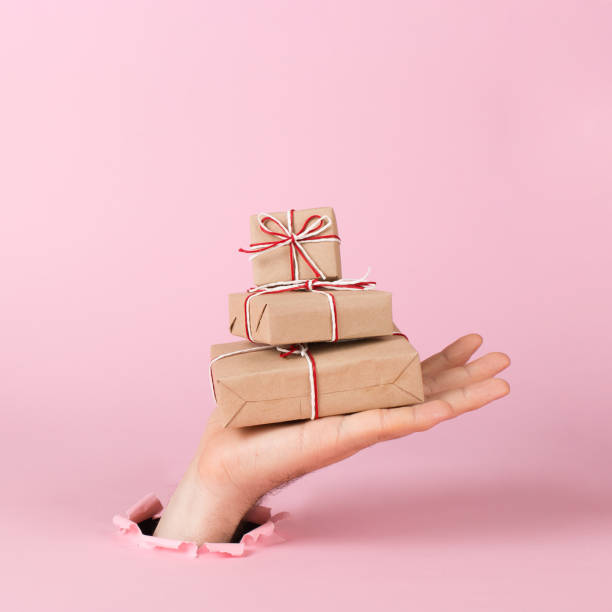 男性の手はピンクの背景に紙の穴から突き出て、工芸品の贈り物の山を保持しています。クリスマスコンセプト、印刷空白、コピースペース。 - birthday card greeting card birthday christmas card ストックフォトと画像