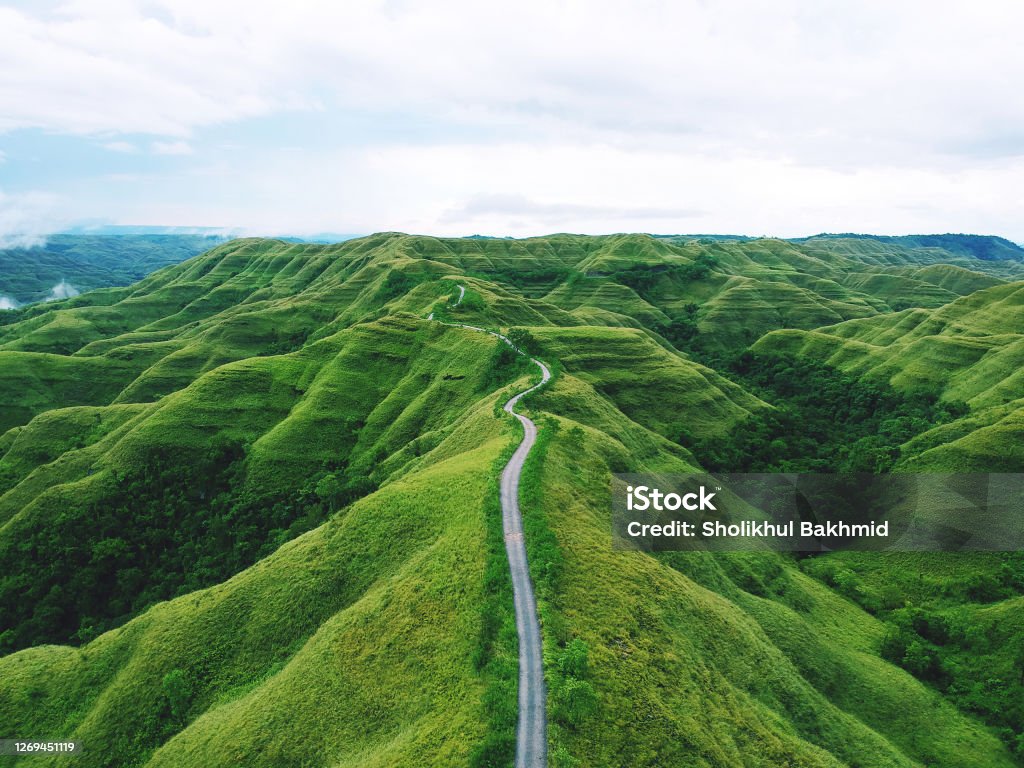 A long winding road between green hills Aerial drone view: A long winding road between hills of green grass in remote parts of the Indonesian island of Sumba Footpath Stock Photo