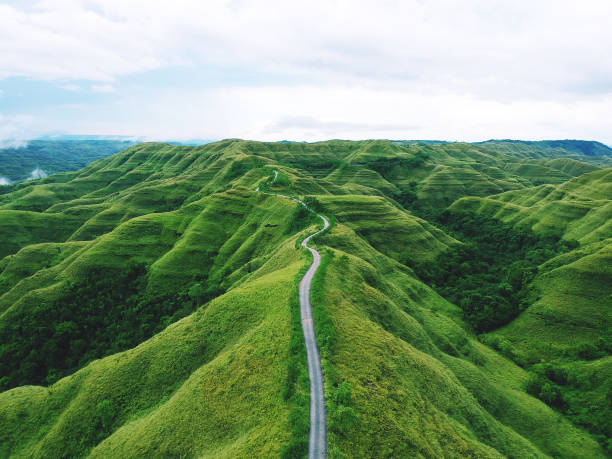 A long winding road between green hills Aerial drone view: A long winding road between hills of green grass in remote parts of the Indonesian island of Sumba winding road photos stock pictures, royalty-free photos & images