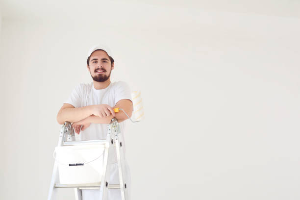A male painter in a white uniform with a roller works in his hand in a white room.