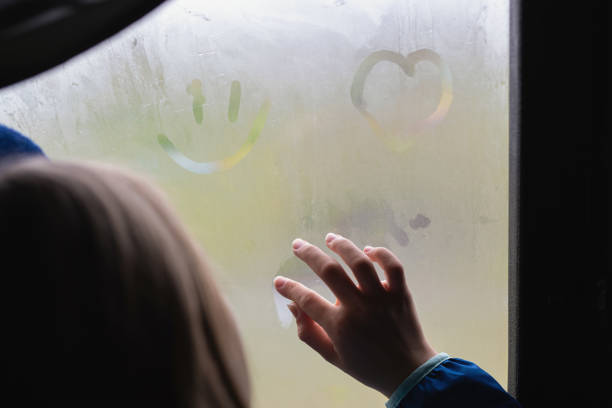 girl or young women hand draws on misted, foggy window. finger on wet glass draws the heart, window and rain stock photo
