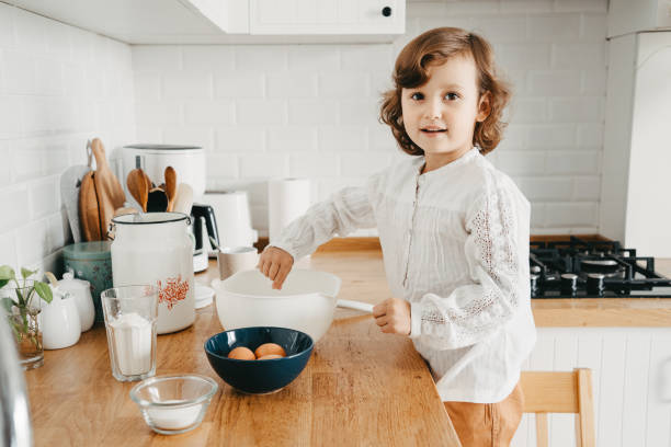 Little girl preparing dough for pancakes at the kitchen. stock photo