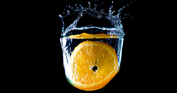 A slice of Orange dropping into water making a splash with a black background.