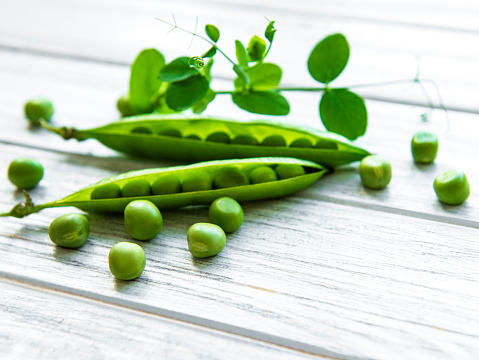 Pods of green peas with pea leaves  on a white wooden background. Organic food.