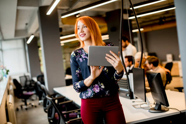 istock Young businesswoman working on digital tablet while in the background team working in the modern office 1269476061