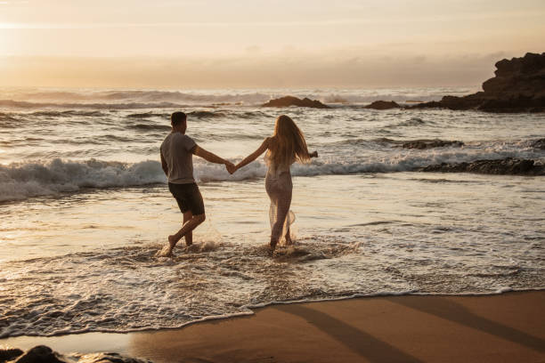 istock Young couple running barefoot on the beach 1269478648