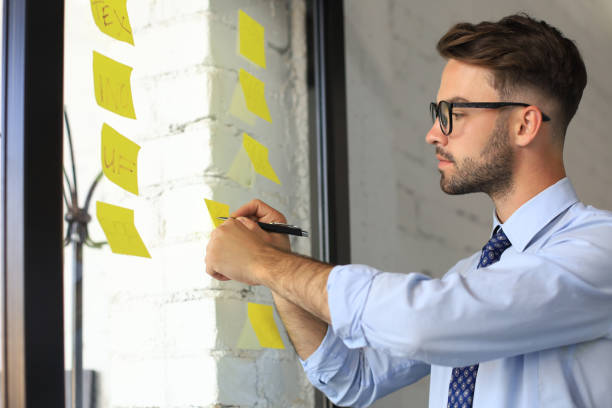 istock Young modern business man using adhesive notes while standing behind the glass wall in the office. 1269484009