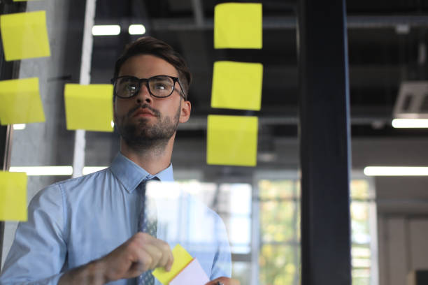 istock Young modern business man using adhesive notes while standing behind the glass wall in the office. 1269484968