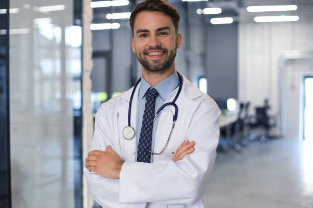 istock Handsome friendly young doctor on hospital corridor looking at camera, smiling. 1269486200