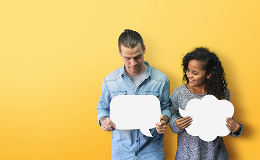 Portrait Hipster African American male and female in casual standing holding and looking at white blank speech bubble over isolated yellow background. Happy Diversity couple holding with smiling face