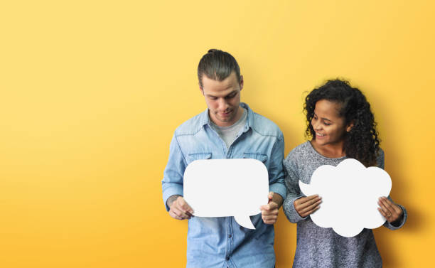 Happy Diversity couple holding white speech bubble on yellow background Portrait Hipster African American male and female in casual standing holding and looking at white blank speech bubble over isolated yellow background. Happy Diversity couple holding with smiling face two people thinking stock pictures, royalty-free photos & images