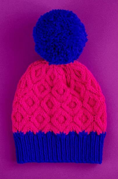 istock Beautiful two color handknitted hat with pompon on purple background. Top view 1269508879