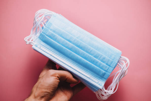 istock Stack of medical protective masks in hand on pink background. 1269510265