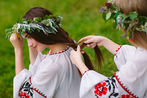Midsummer. Two girls in the Slavic clothes weave braids in the hair near the fire.