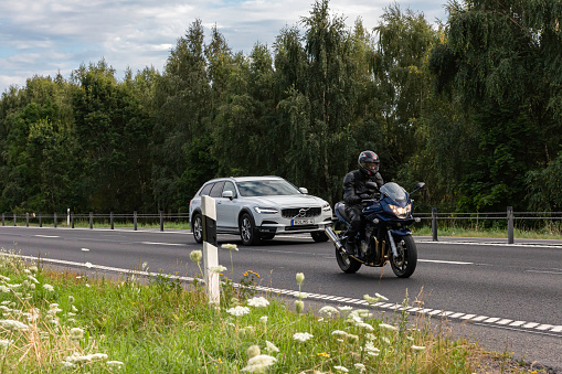 Motala Sweden August 2020\nmotorbike driving infront of a white volvo car with lush surroundings