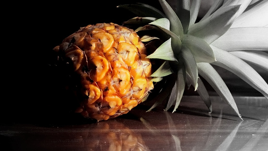 Single one full whole organic pineapple fruit on wooden background ripe fully grown mature, laid down reflect on the side.